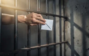 Une main tient un papier plié derrière des barreaux de prison avec des rayons de lumière projetant des ombres.